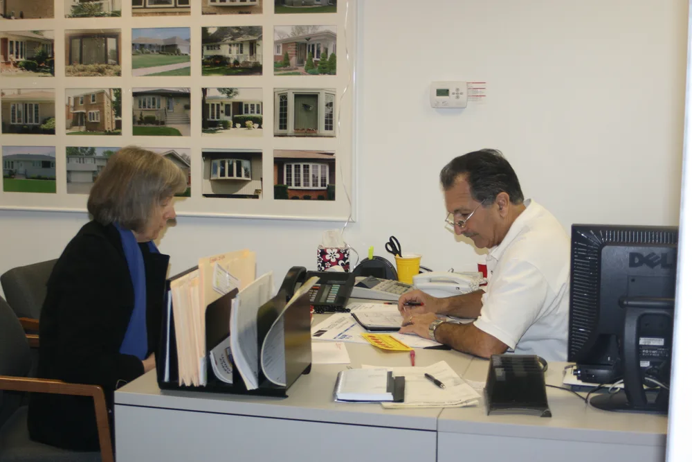 An Excel rep going over a project with a customer at the office, past jobs pinned on the wall behind.