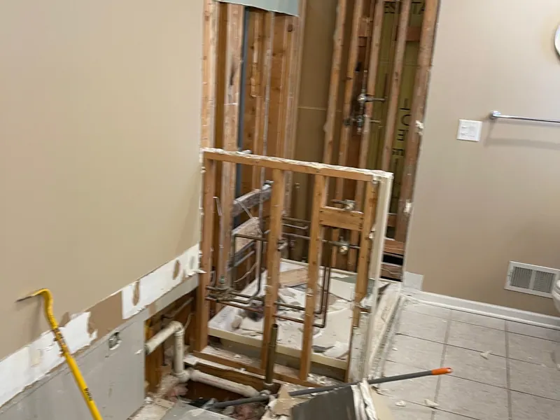 A bathroom mid-remodel with the walls opened to the studs and plumbing exposed — Excel repairs what's behind the wall before finishing
