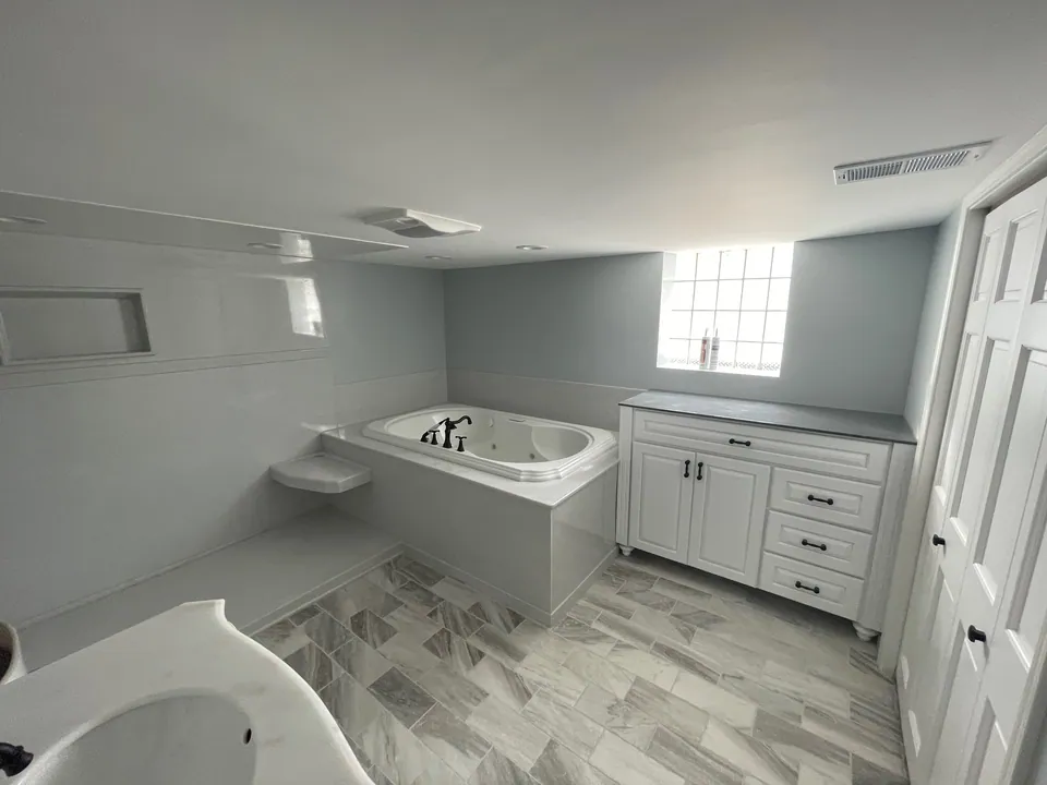 Full bathroom remodel with a drop-in jetted tub on a solid-surface deck, a white shaker vanity with matte-black hardware, and gray wood-look tile floor, Chicagoland