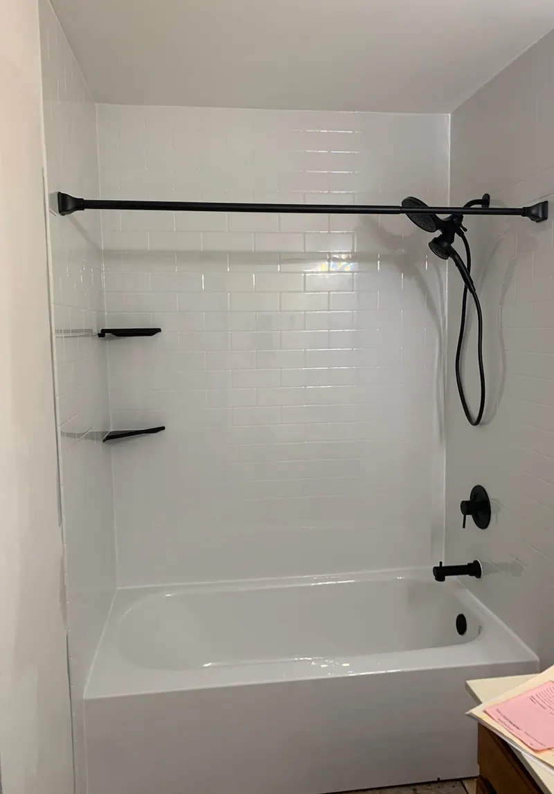 Finished Excel tub-and-shower with white subway-pattern solid-surface walls and matte-black fixtures
