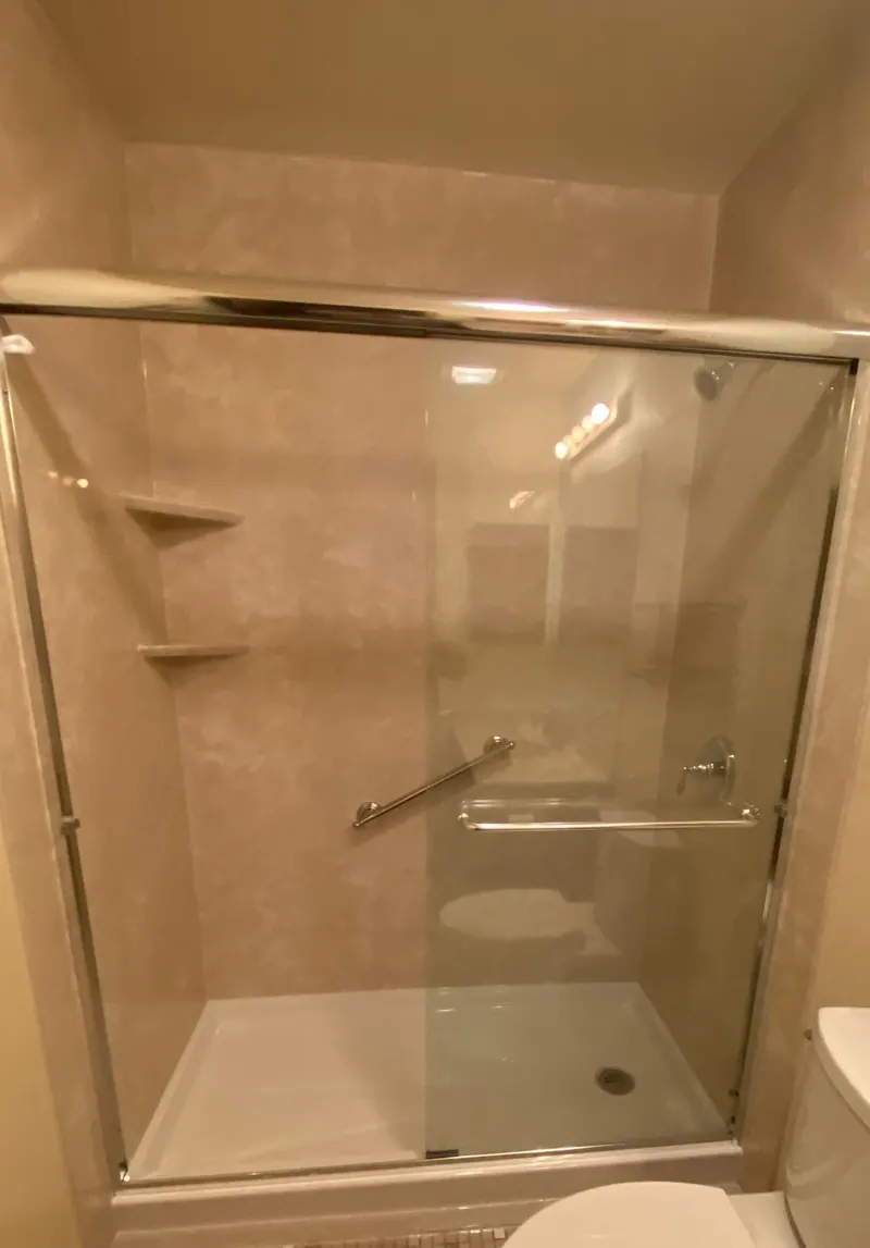 After — a new solid-surface walk-in shower with sliding glass doors and a grab bar, an Excel install