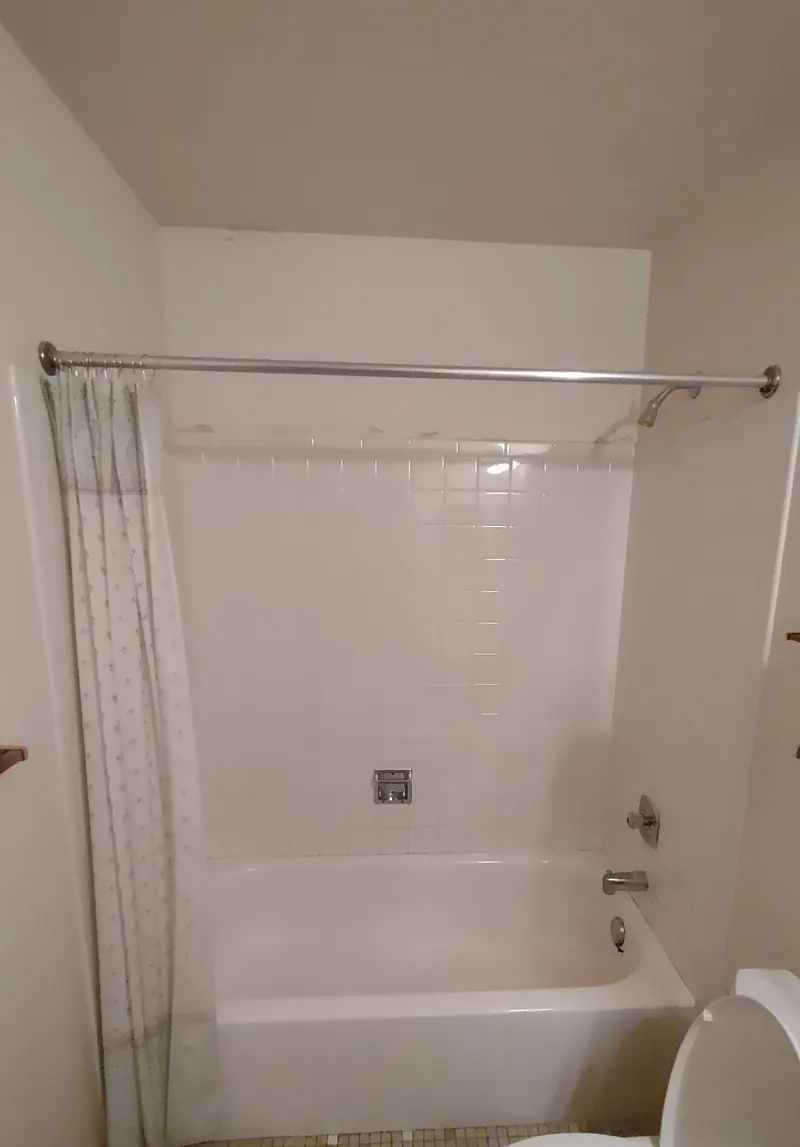 Before — the original white-tile tub-and-shower combo with a shower curtain