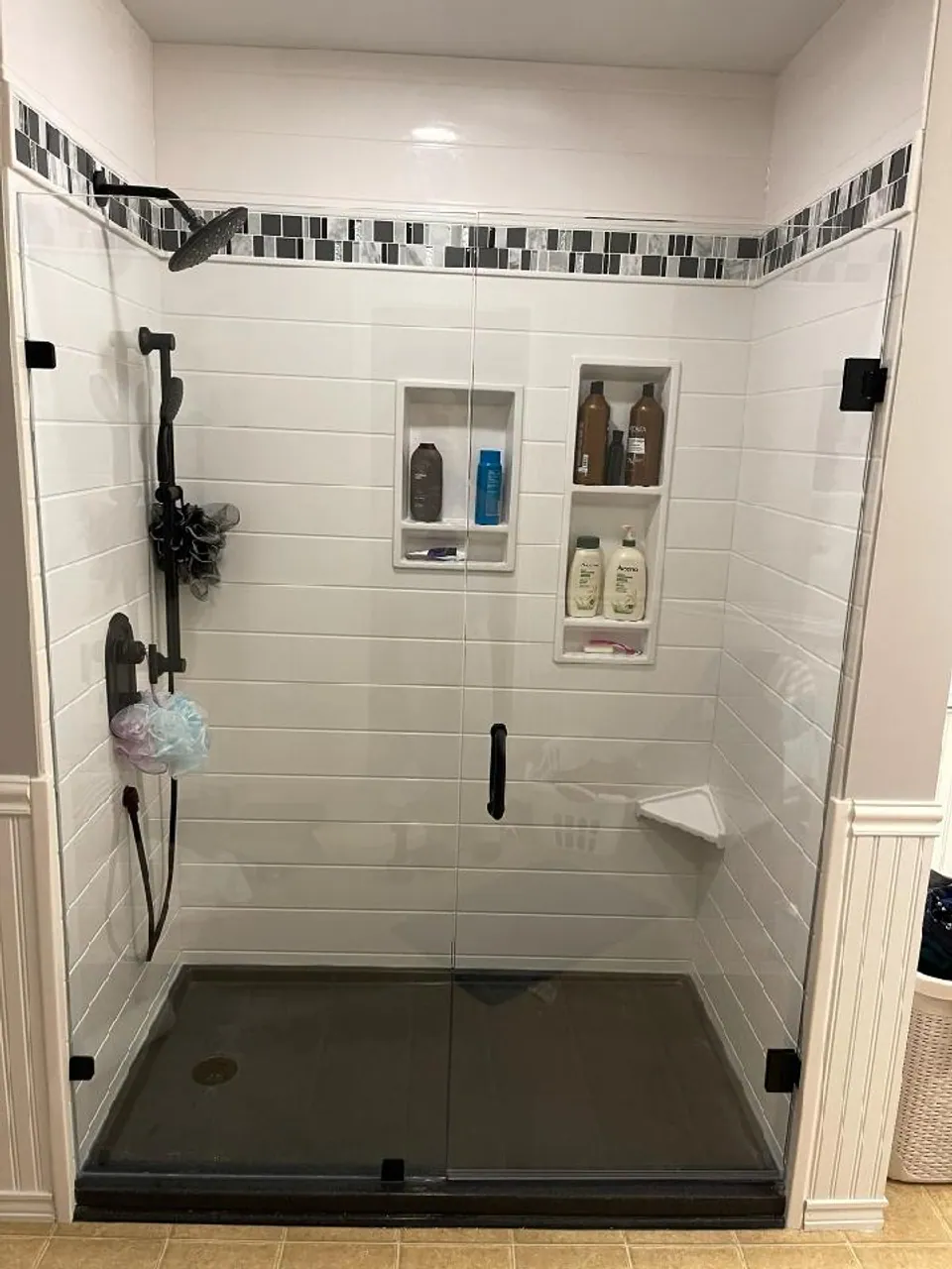Frameless-glass walk-in shower with white shiplap-textured solid-surface walls, a black mosaic accent band, dual niches, a corner seat, and oil-rubbed bronze fixtures, Chicagoland south suburbs