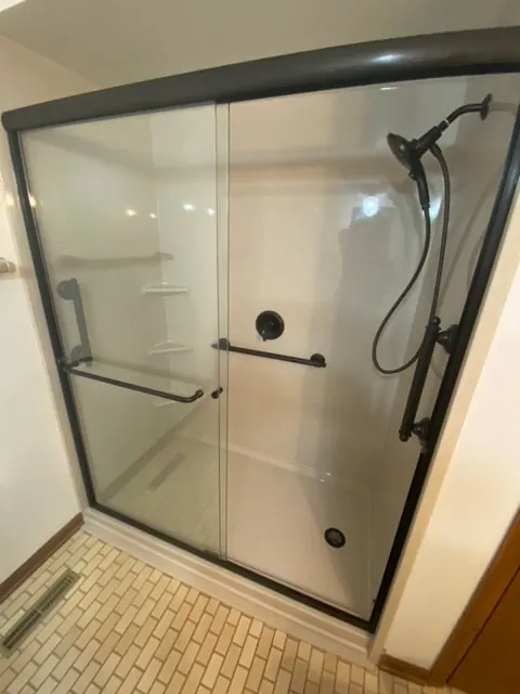 Walk-in shower with a black-framed glass enclosure, an Excel install