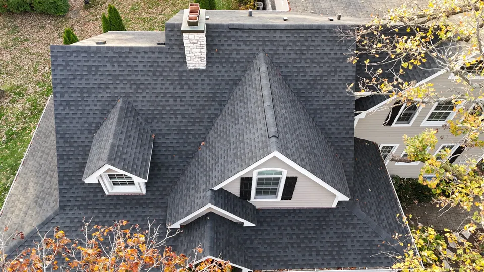 An aerial drone view of a new charcoal asphalt-shingle roof with dormers and a stone chimney on a Chicagoland south-suburb home — an Excel install